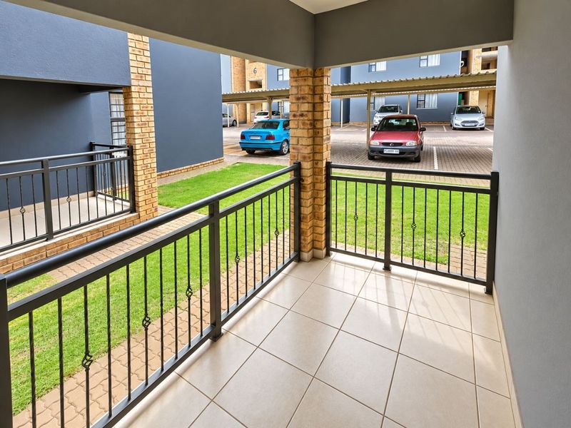 A covered ground-floor patio featuring tiled flooring and a metal balustrade, overlooking a communal garden and parking area.