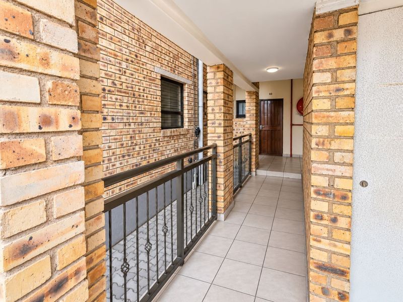 A covered entrance walkway featuring face brick pillars, tiled flooring, and a secure metal balustrade leading to the front door.