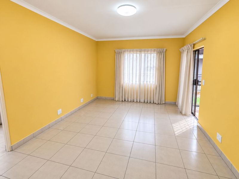 A bright, empty living room featuring tiled flooring, yellow walls, and a sliding glass door providing access to the exterior.