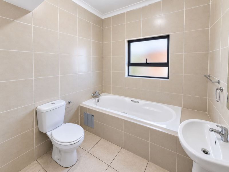A clean, well-maintained bathroom featuring neutral wall and floor tiles, a built-in bathtub, a pedestal basin, and a toilet.
