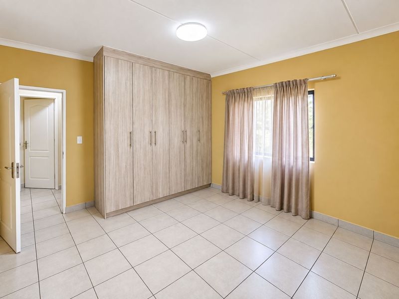 A bright, empty bedroom featuring neutral tiled flooring, built-in wooden cupboards, and a window with curtain rails.