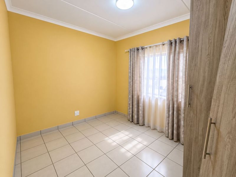 A bright, empty bedroom featuring neutral tiled flooring, built-in cupboards, and yellow painted walls, offering a clean and versatile space.