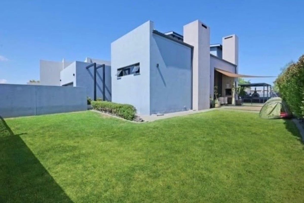 Rear view of a modern house featuring a well-maintained lawn, boundary wall, and a covered patio area with a built-in braai.