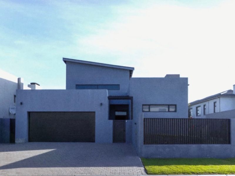 Modern contemporary home featuring a clean grey facade, integrated garage, paved driveway, and secure boundary wall with slatted fencing.