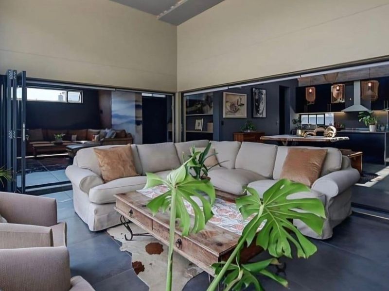 Spacious open-plan living area featuring large bi-fold doors that open to an outdoor space, seamlessly connecting to a modern kitchen with dark cabinetry.