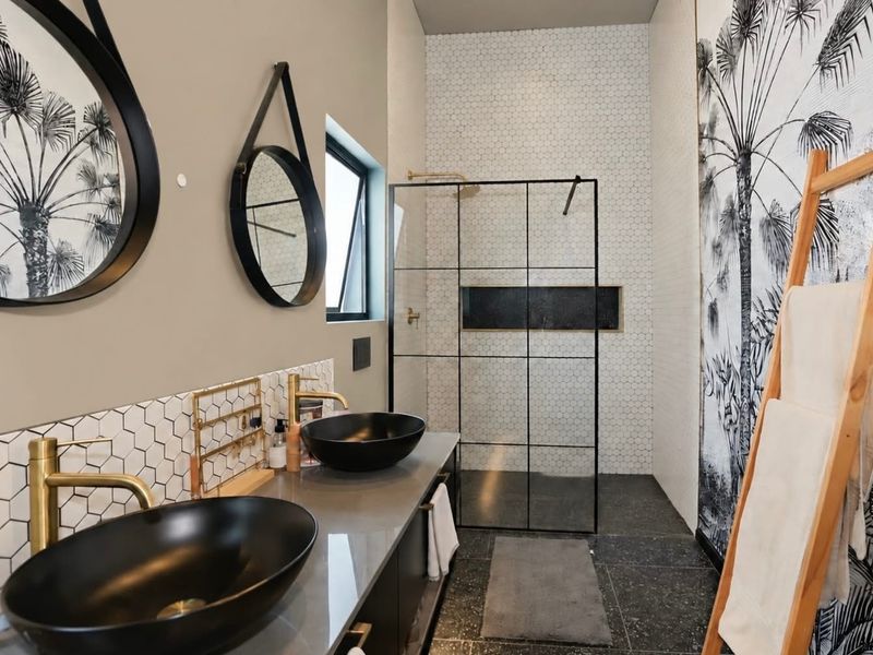 Modern bathroom featuring a double vanity with vessel sinks, brass fixtures, and a spacious walk-in shower with a black-framed glass screen.