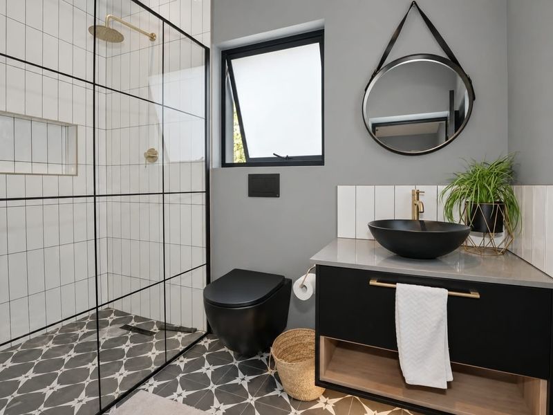 Modern bathroom featuring a walk-in shower with black-framed glass, wall-hung toilet, vessel sink on a vanity cabinet, and stylish patterned floor tiles.