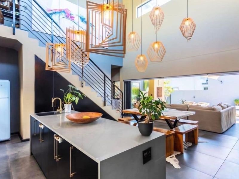 Modern open-plan living area featuring a sleek kitchen island, contemporary pendant lighting, and a striking staircase, seamlessly flowing to an outdoor patio space.