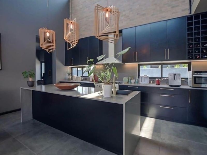 Modern kitchen featuring dark cabinetry, a large central island with stone countertops, integrated appliances, and high ceilings with feature pendant lighting.