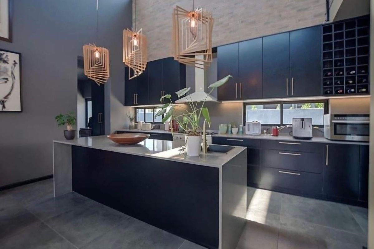 Modern kitchen featuring dark cabinetry, a large central island with stone countertops, integrated appliances, and high ceilings with feature pendant lighting.