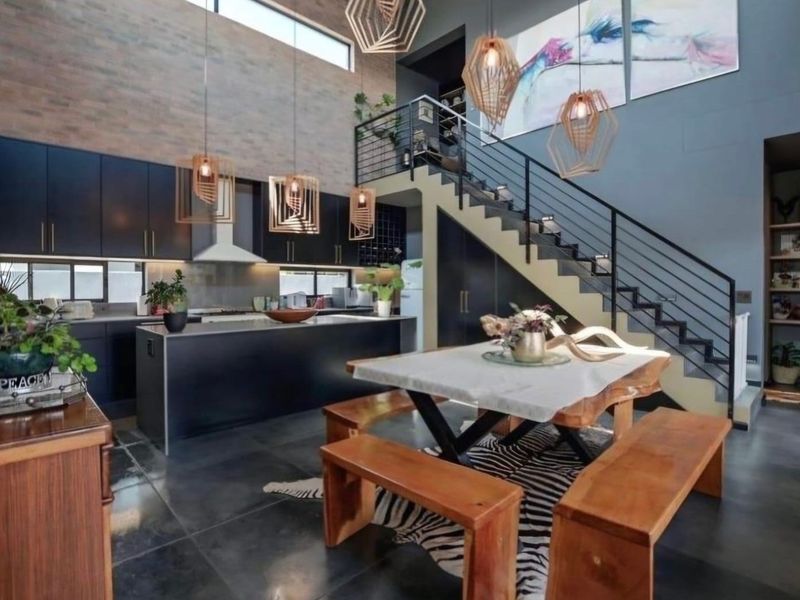 Modern open-plan living area featuring a sleek kitchen with dark cabinetry, a central island, and a striking staircase with metal balustrades.