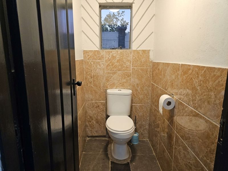 A compact guest bathroom featuring floor-to-ceiling marble-look wall tiles, dark floor tiles, and a standard white toilet.