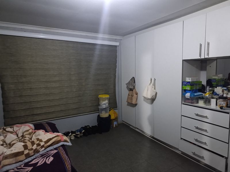 A bedroom featuring extensive built-in white cabinetry, tiled flooring, and modern roller blinds, offering ample storage space.