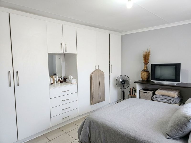 A well-maintained bedroom featuring extensive white built-in cupboards with an integrated vanity and tiled flooring.