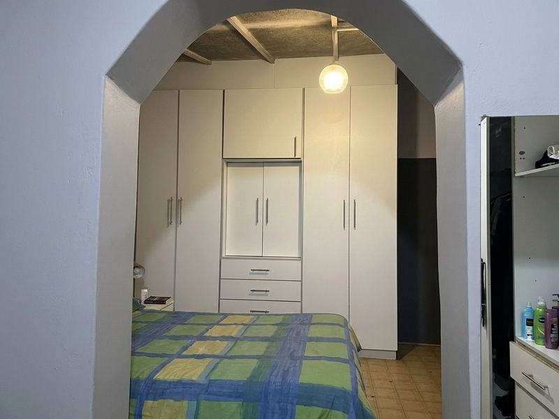 Bedroom featuring built-in cupboards, an arched entryway, and exposed ceiling beams, providing a functional storage solution.