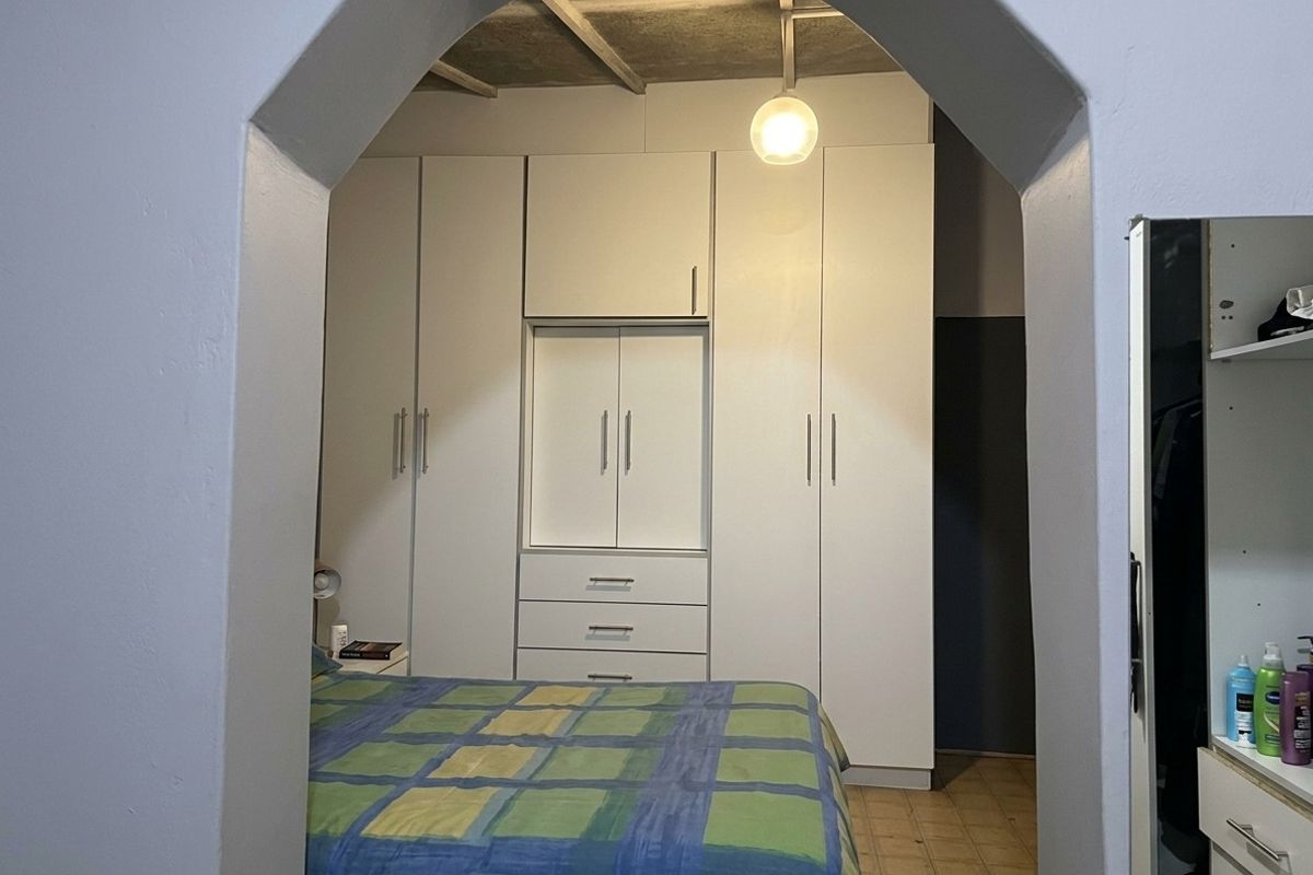 Bedroom featuring built-in cupboards, an arched entryway, and exposed ceiling beams, providing a functional storage solution.