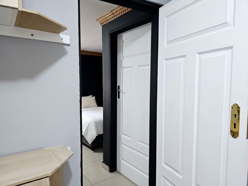 A view through a hallway featuring white panelled doors, contrasting dark door frames, decorative ceiling cornicing, and neutral tiled flooring.