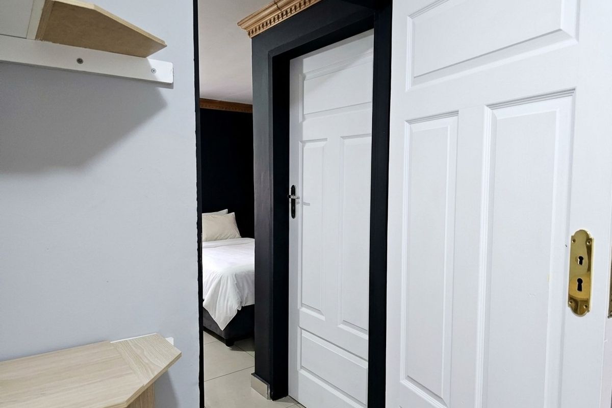 A view through a hallway featuring white panelled doors, contrasting dark door frames, decorative ceiling cornicing, and neutral tiled flooring.