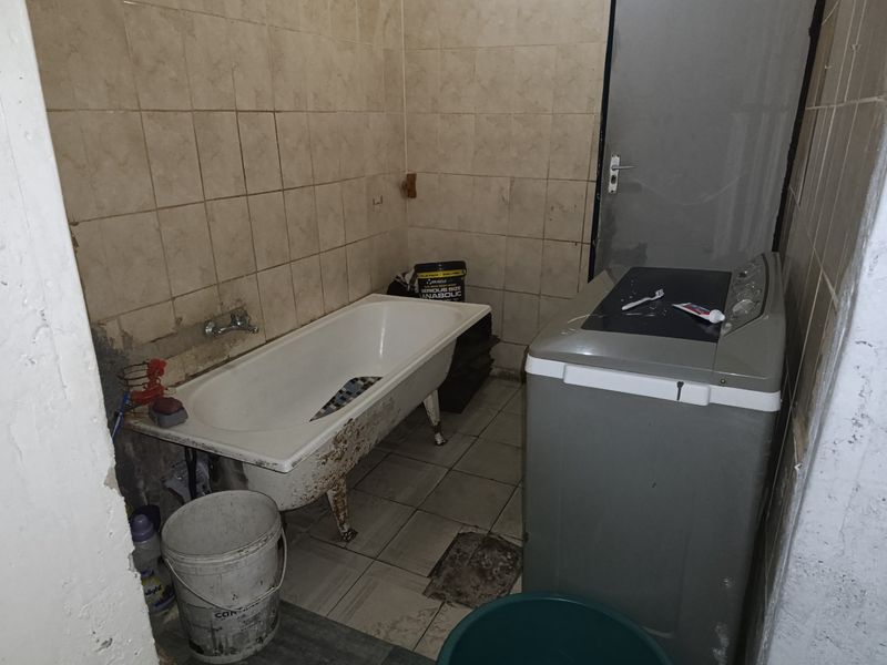 A dated bathroom featuring a freestanding bathtub and tiled surfaces, requiring significant renovation and cosmetic updates to improve functionality and aesthetic appeal.