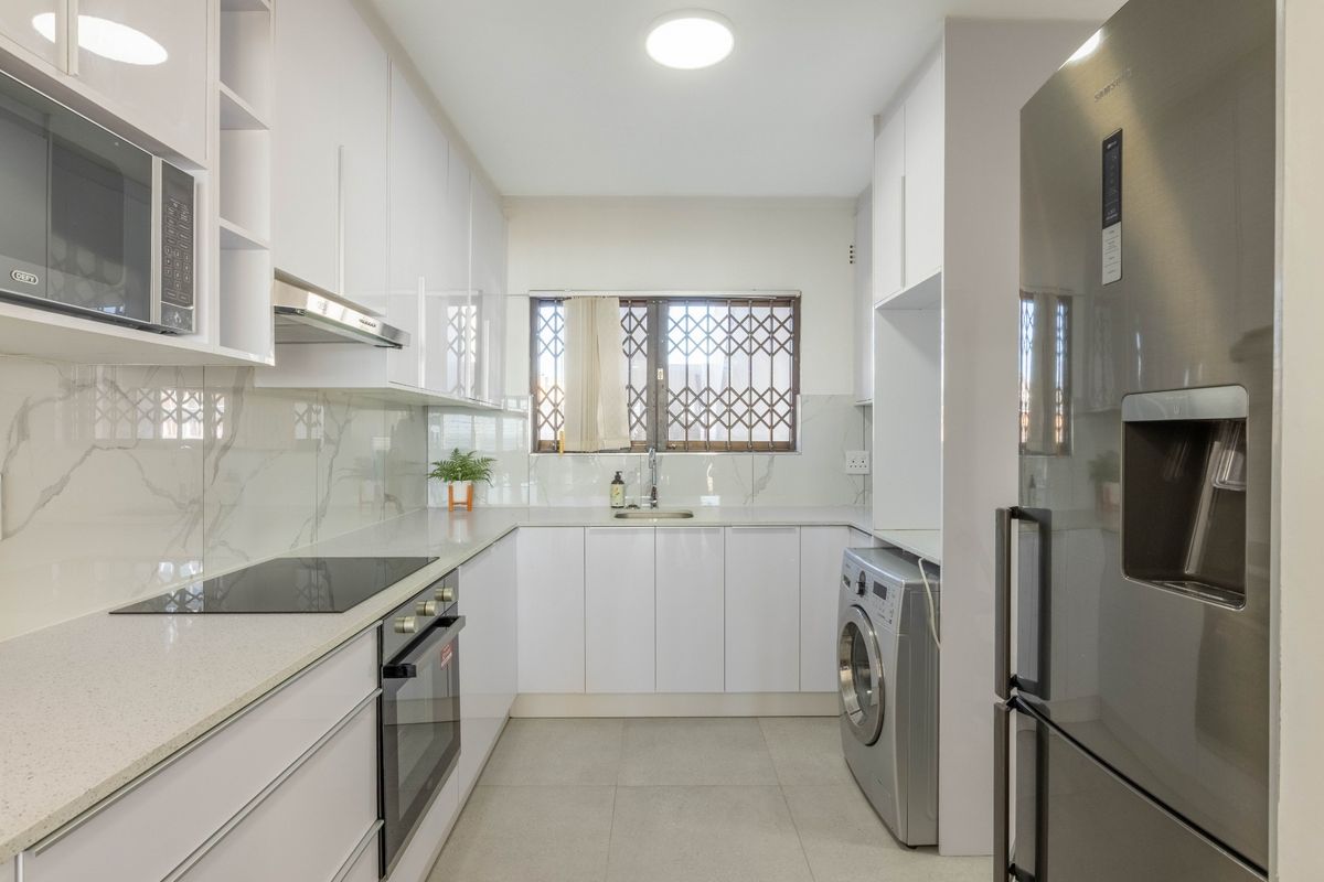 Modern kitchen featuring white high-gloss cabinetry, stone countertops, integrated appliances, and a sleek tiled floor with a window security gate.