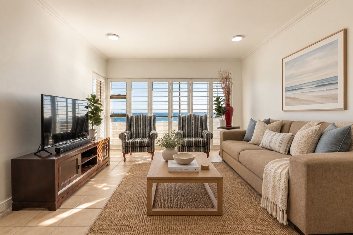 A bright and well-maintained living room featuring tiled flooring, crown molding, and plantation shutters with a view of the ocean.