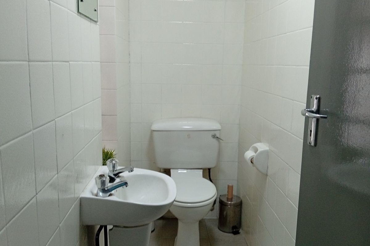 A compact, functional bathroom featuring white ceramic wall tiles, a standard toilet, and a wall-mounted basin with chrome fixtures.