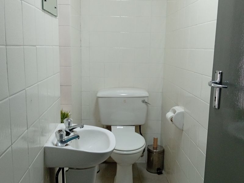A compact, functional bathroom featuring white ceramic wall tiles, a standard toilet, and a wall-mounted basin with chrome fixtures.