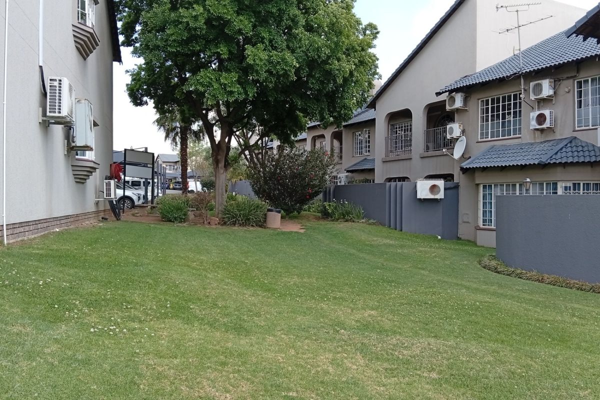 A well-maintained communal lawn area situated between residential building blocks, featuring mature landscaping and exterior wall-mounted air conditioning units.