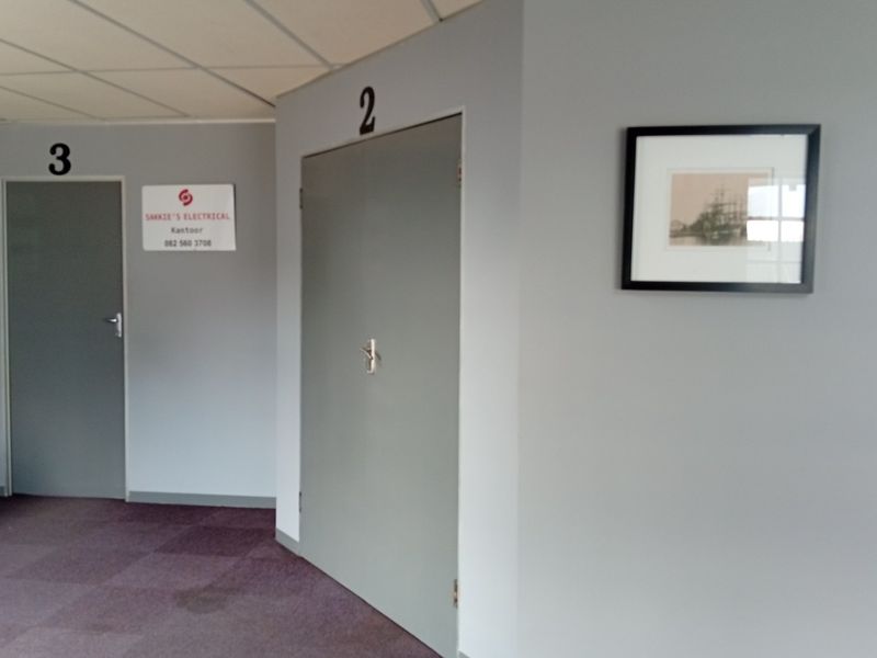 A commercial hallway featuring numbered office doors, a wall-mounted electrical distribution board, and neutral grey wall finishes.