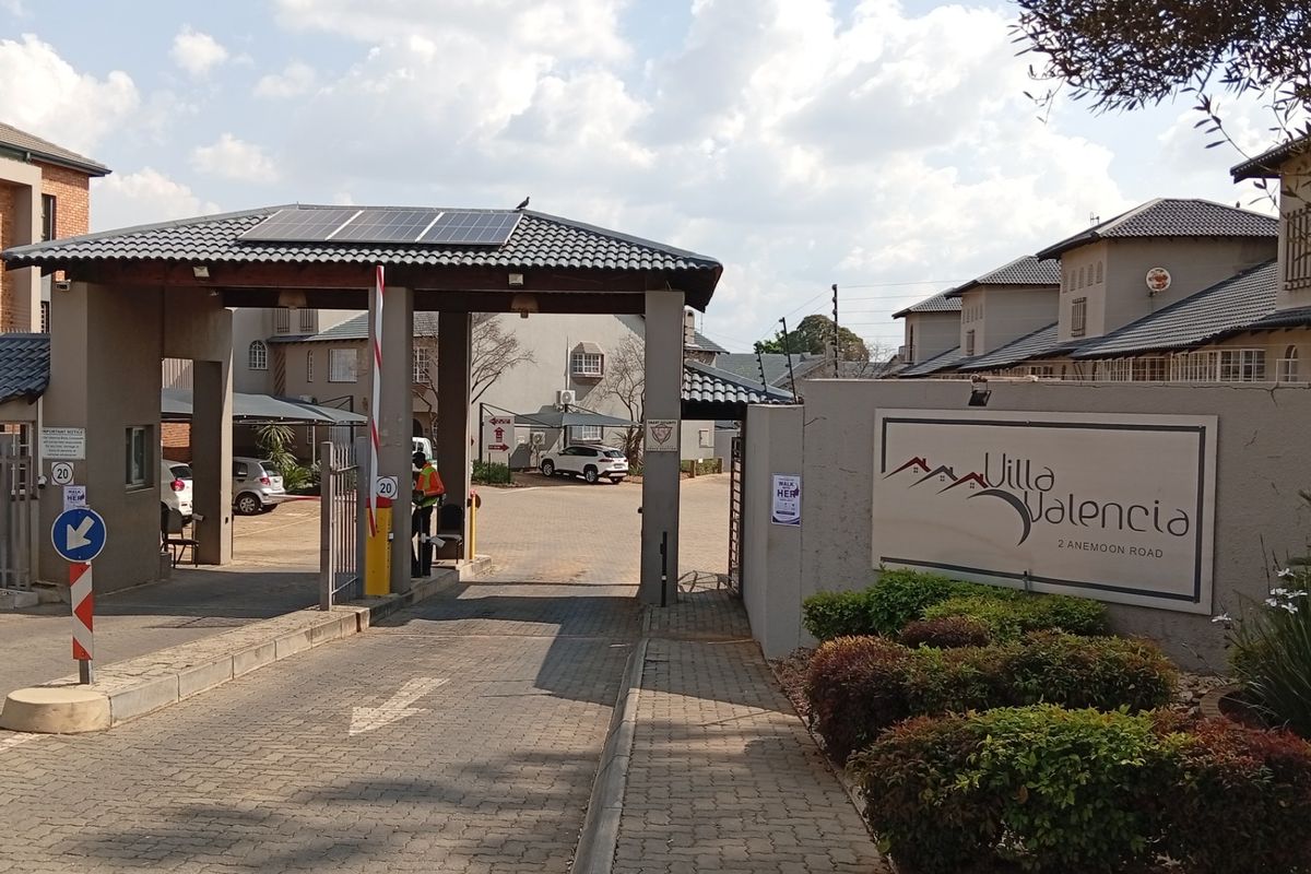 The secure entrance to Villa Valencia complex, featuring a gated access point, boom gate, and professional signage.