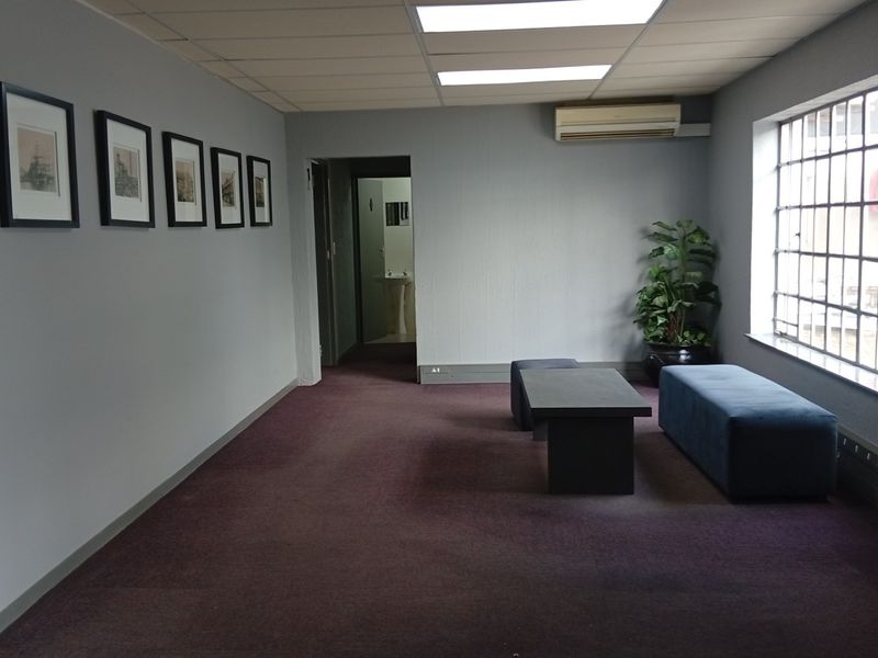 A functional office space featuring a suspended ceiling, recessed lighting, split-system air conditioning, and security bars on the windows.