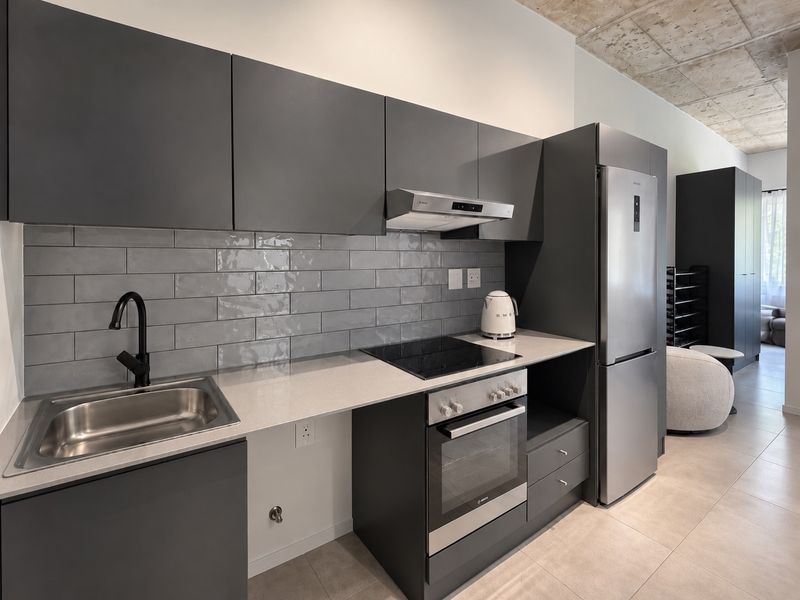 Modern kitchen featuring dark grey cabinetry, stone countertops, subway tile backsplash, integrated appliances, and an industrial-style exposed concrete ceiling.