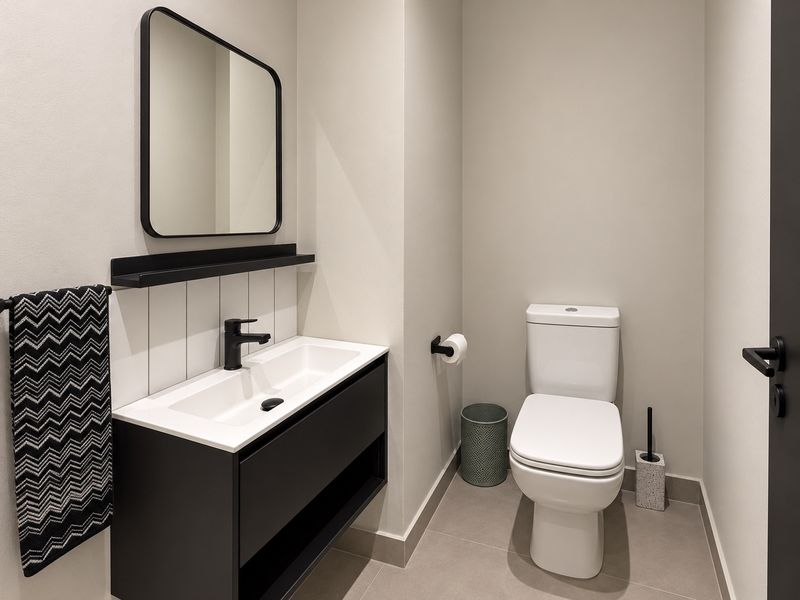 A modern, well-maintained bathroom featuring a sleek wall-mounted vanity with integrated basin, black fixtures, and neutral tiling.