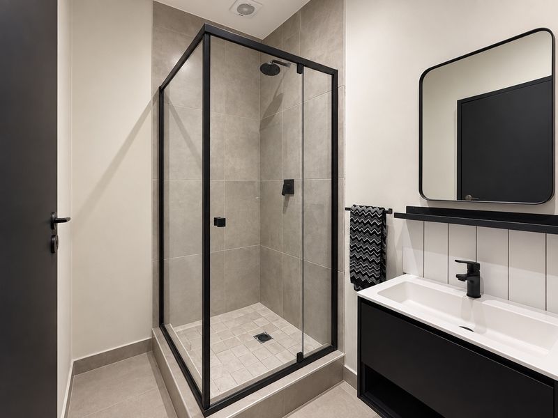 Modern bathroom featuring a walk-in shower with black frame, contemporary vanity unit with integrated basin, and sleek black fixtures.