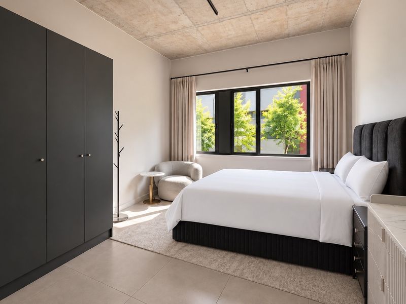 Modern bedroom featuring an exposed concrete ceiling, large black-framed windows, tiled flooring, and a sleek built-in wardrobe.