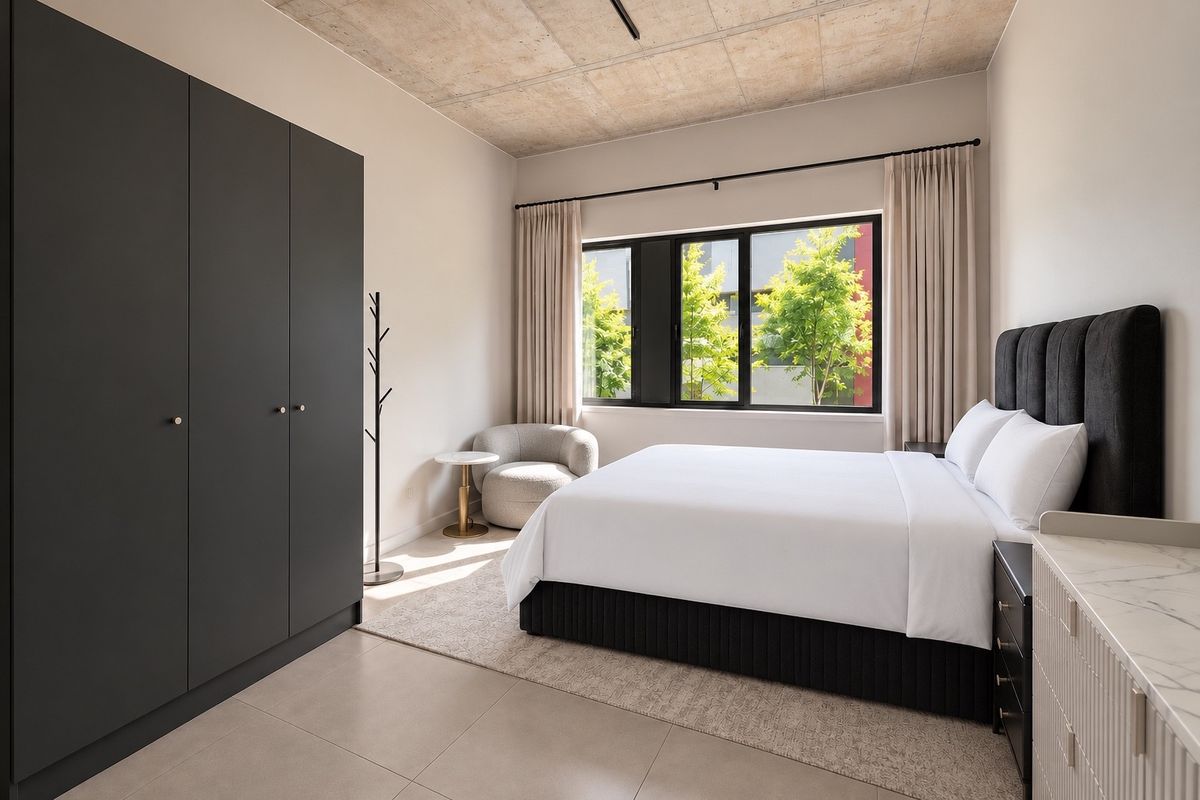 Modern bedroom featuring an exposed concrete ceiling, large black-framed windows, tiled flooring, and a sleek built-in wardrobe.
