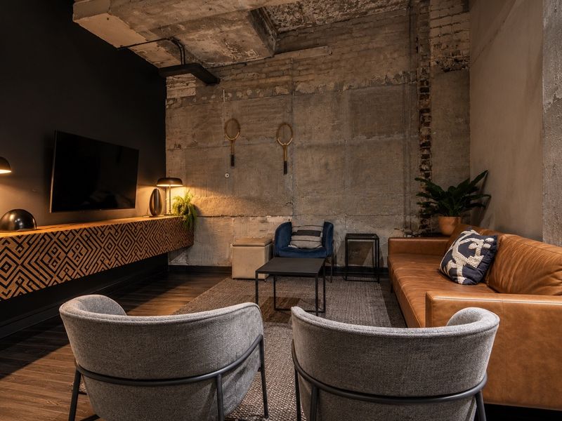 Modern industrial-style living room featuring exposed concrete ceilings, raw brick walls, and a custom built-in floating media console with dark hardwood flooring.