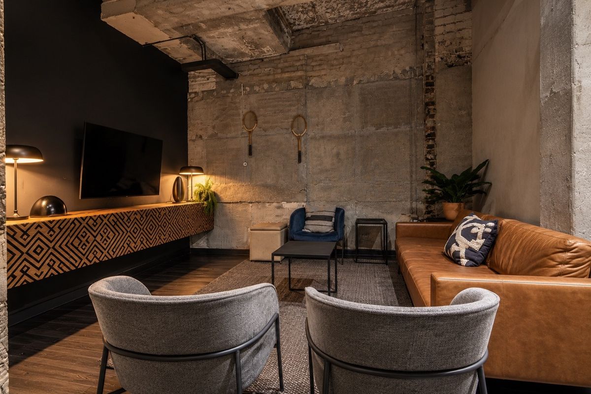 Modern industrial-style living room featuring exposed concrete ceilings, raw brick walls, and a custom built-in floating media console with dark hardwood flooring.