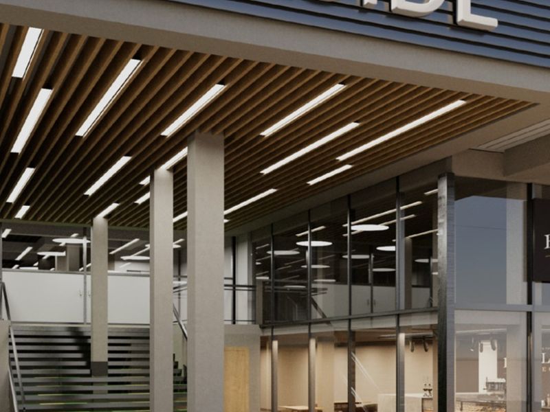 Modern commercial building entrance featuring a slatted timber ceiling, recessed lighting, and a prominent glass facade with a staircase.