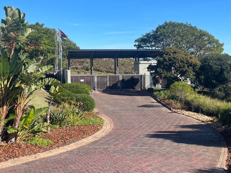 A well-maintained entrance to the property featuring a paved driveway, secure gated access, and established landscaping.