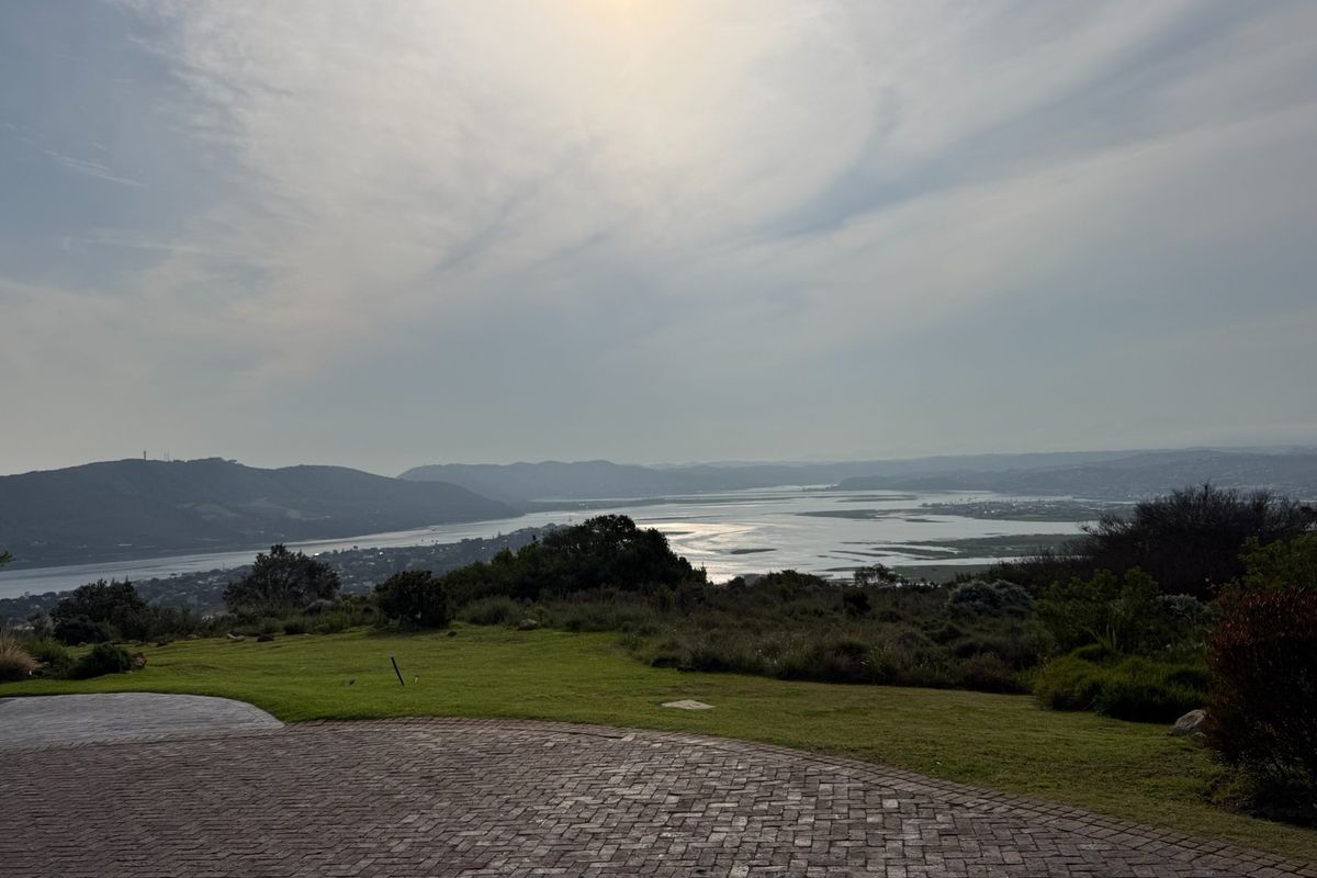 A scenic elevated view overlooking a river estuary and surrounding hills, featuring a paved driveway and well-maintained lawn in the foreground.