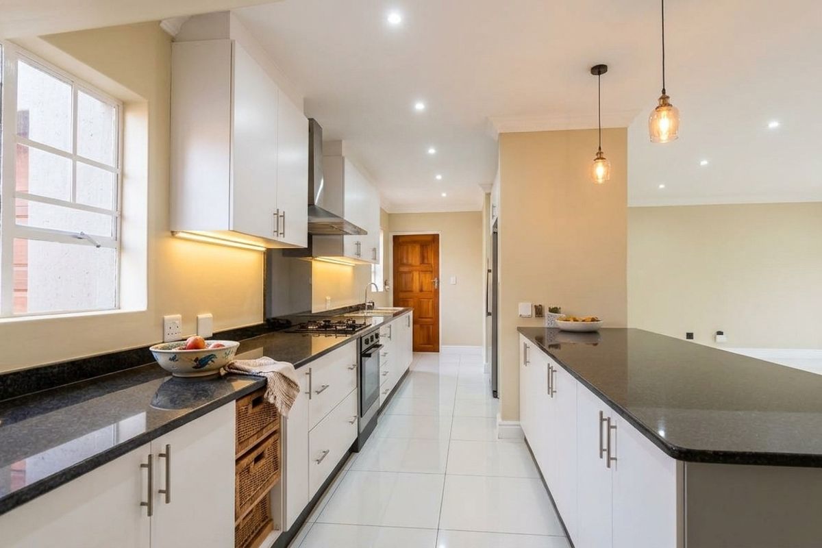 Modern kitchen featuring sleek white cabinetry, dark granite countertops, integrated appliances, and stylish pendant lighting, flowing into an open-plan living area.