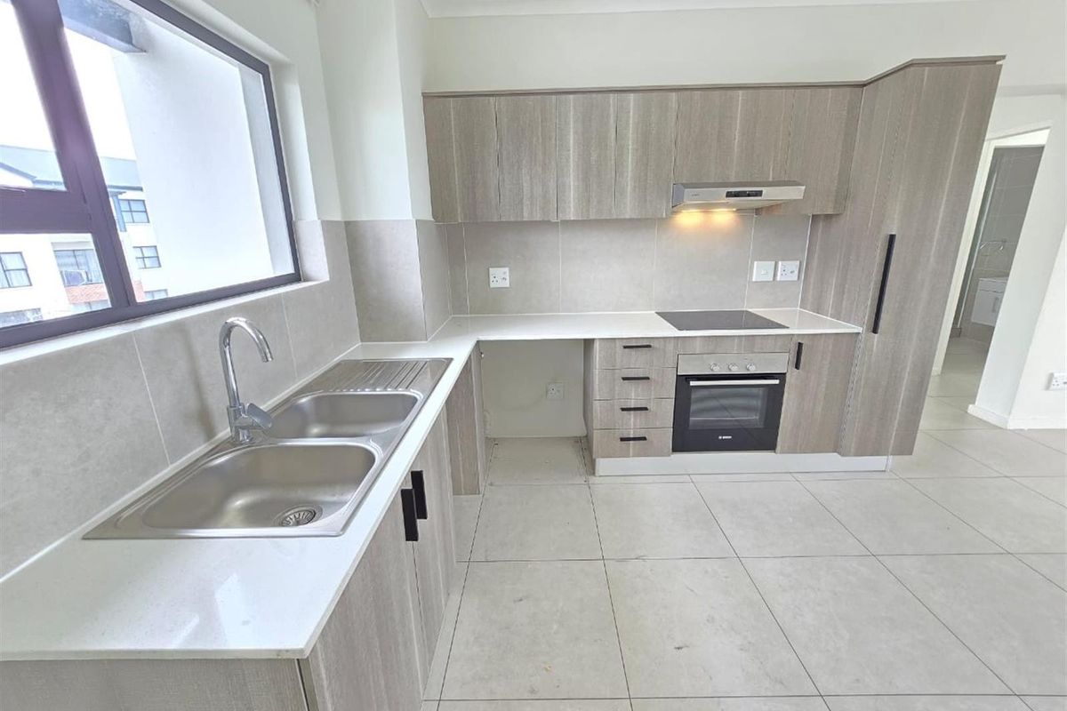 Modern kitchen featuring light wood-grain cabinetry, stone countertops, a double basin sink, and integrated appliances including an oven and electric hob.