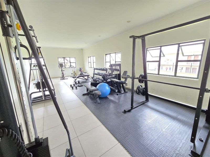 A spacious residential gym featuring tiled and rubber flooring, multiple windows for natural light, and recessed ceiling lighting.