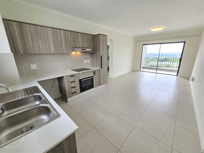 Modern open-plan kitchen and living area featuring sleek cabinetry, built-in appliances, tiled floors, and direct access to a balcony with scenic views.