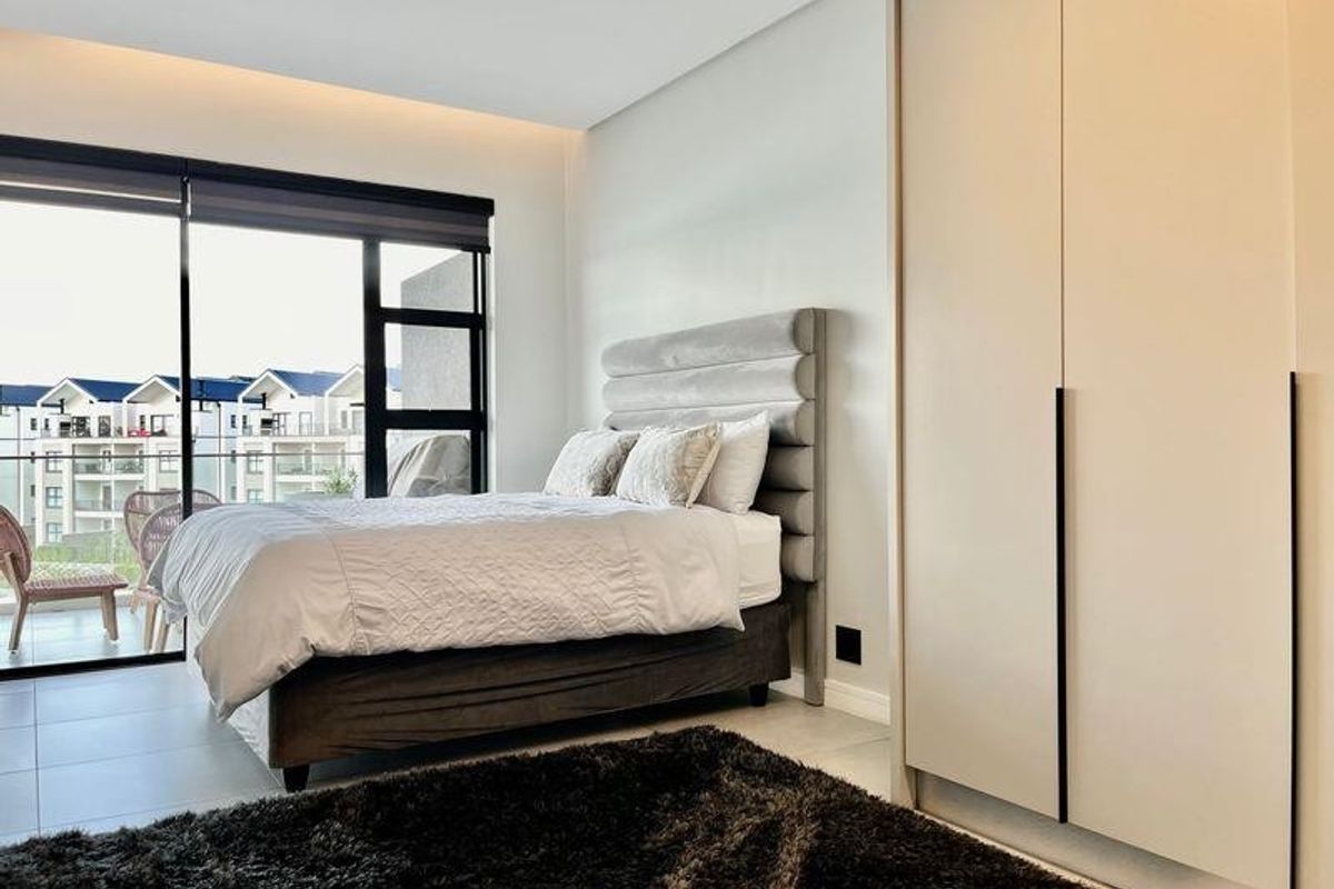 Modern bedroom featuring built-in wardrobes, tiled flooring, and large sliding glass doors providing access to a private balcony.