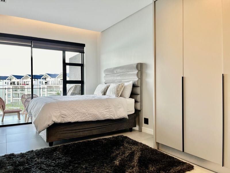 Modern bedroom featuring built-in wardrobes, tiled flooring, and large sliding glass doors providing access to a private balcony.