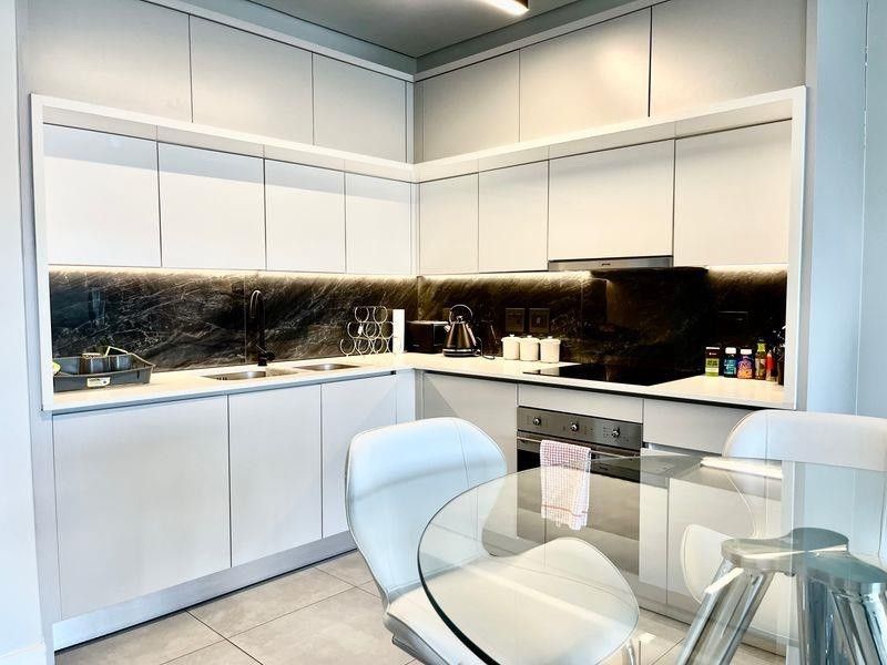 Modern kitchen featuring sleek white cabinetry, dark marble-look backsplash, integrated appliances, and high-quality stone countertops with under-cabinet lighting.