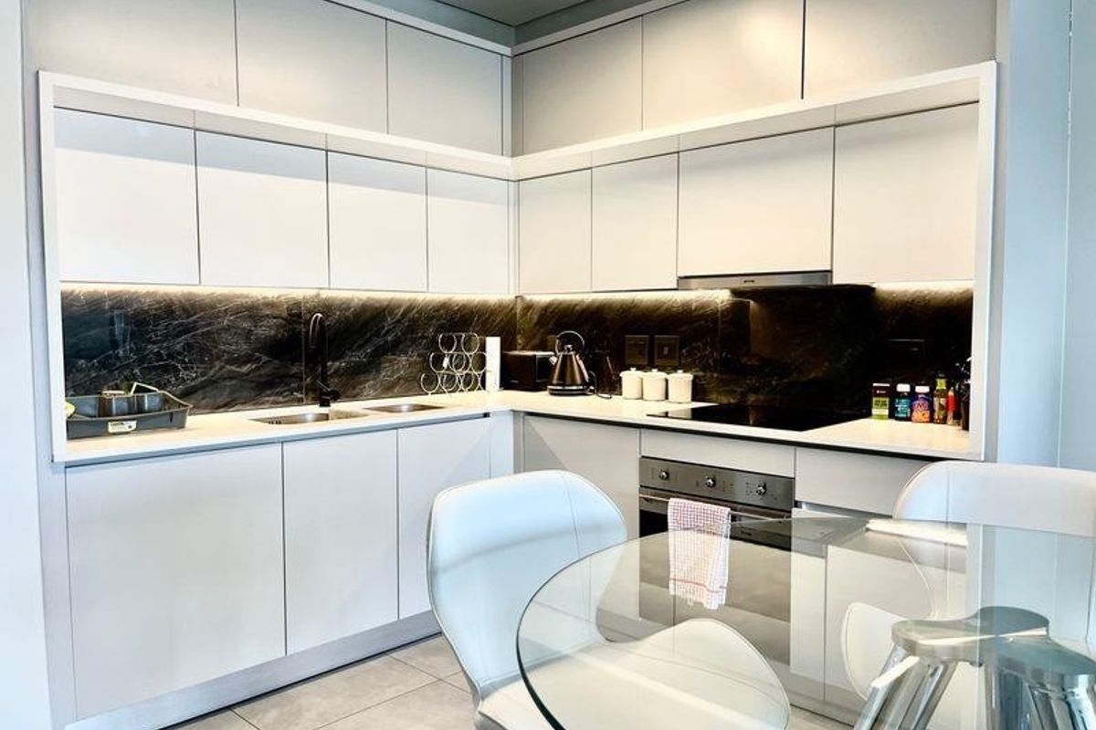 Modern kitchen featuring sleek white cabinetry, dark marble-look backsplash, integrated appliances, and high-quality stone countertops with under-cabinet lighting.
