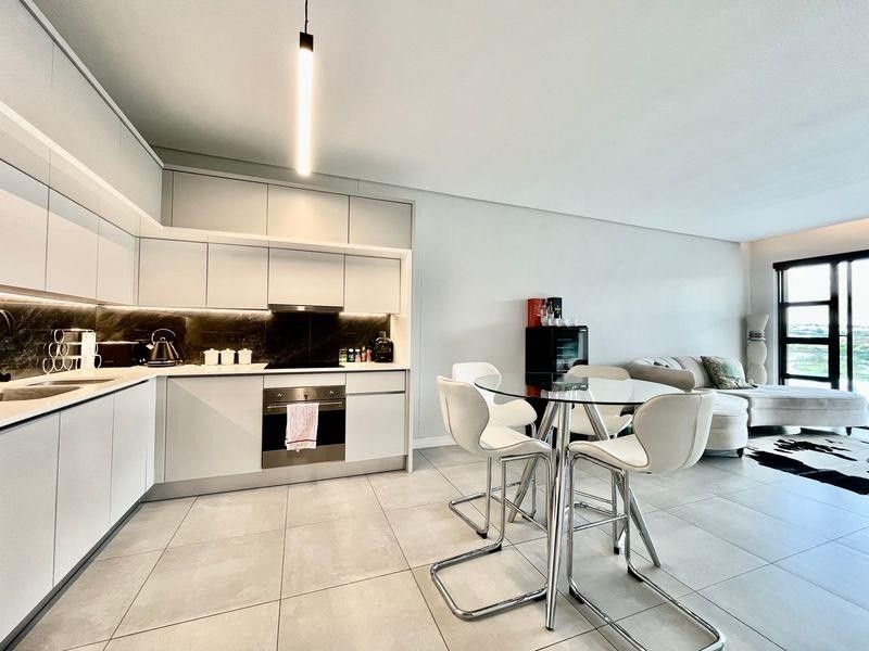 Modern open-plan apartment featuring a sleek kitchen with integrated appliances, stone tile flooring, and seamless flow to a bright living area with balcony access.